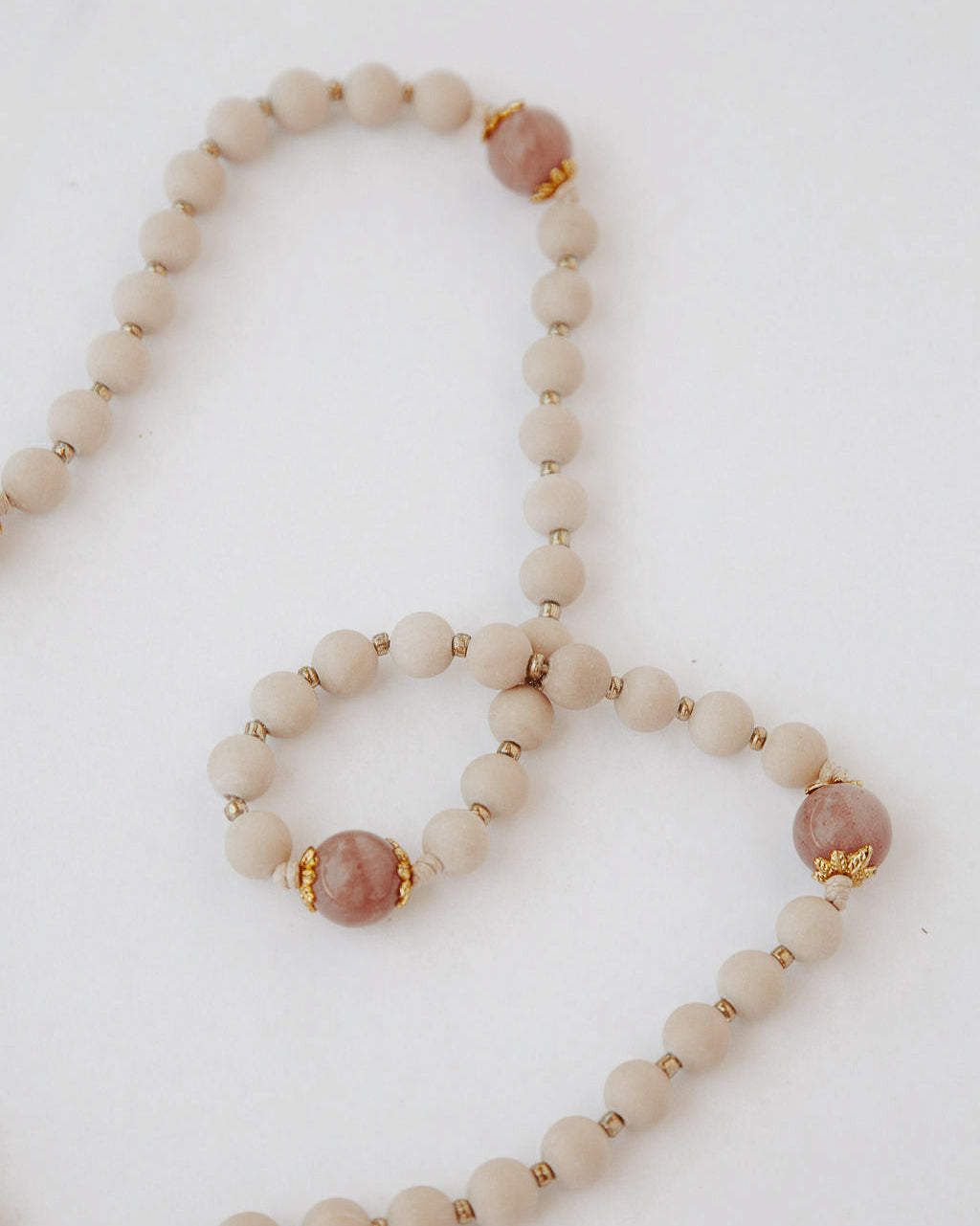 Rosary with beige and pink beads and a gold details on a light background