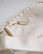Close-up of a cream belt bag with a zipper on a light gray background
