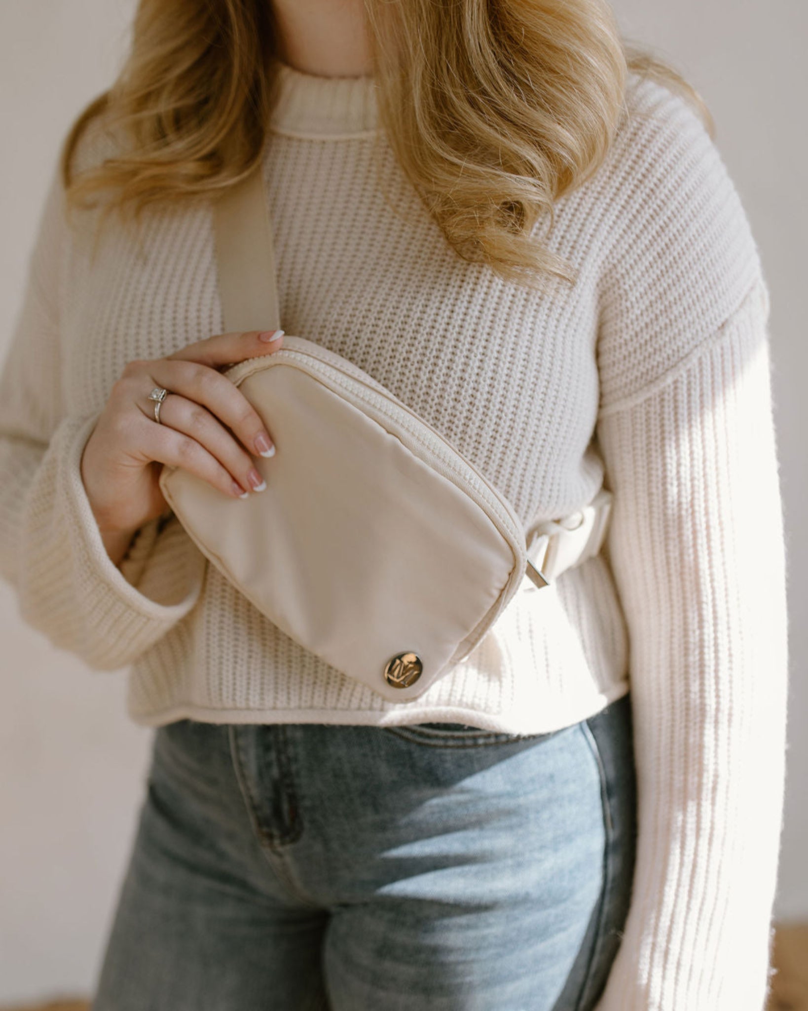  Woman wearing cream marian belt bag and holding against a neutral background