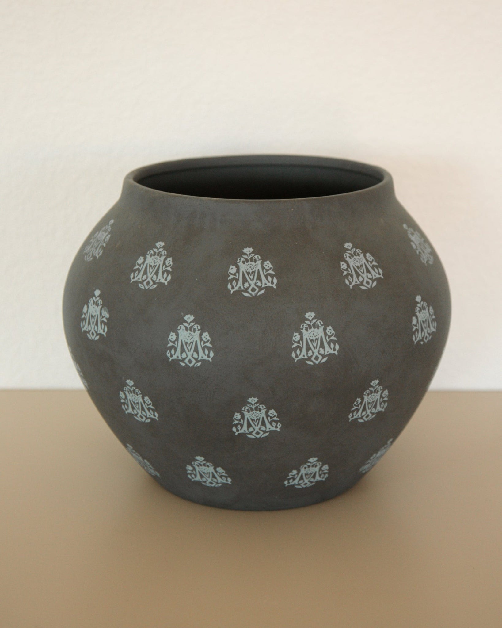 A dark grey Marian Vase with light blue Marian "M" symbols all over. 