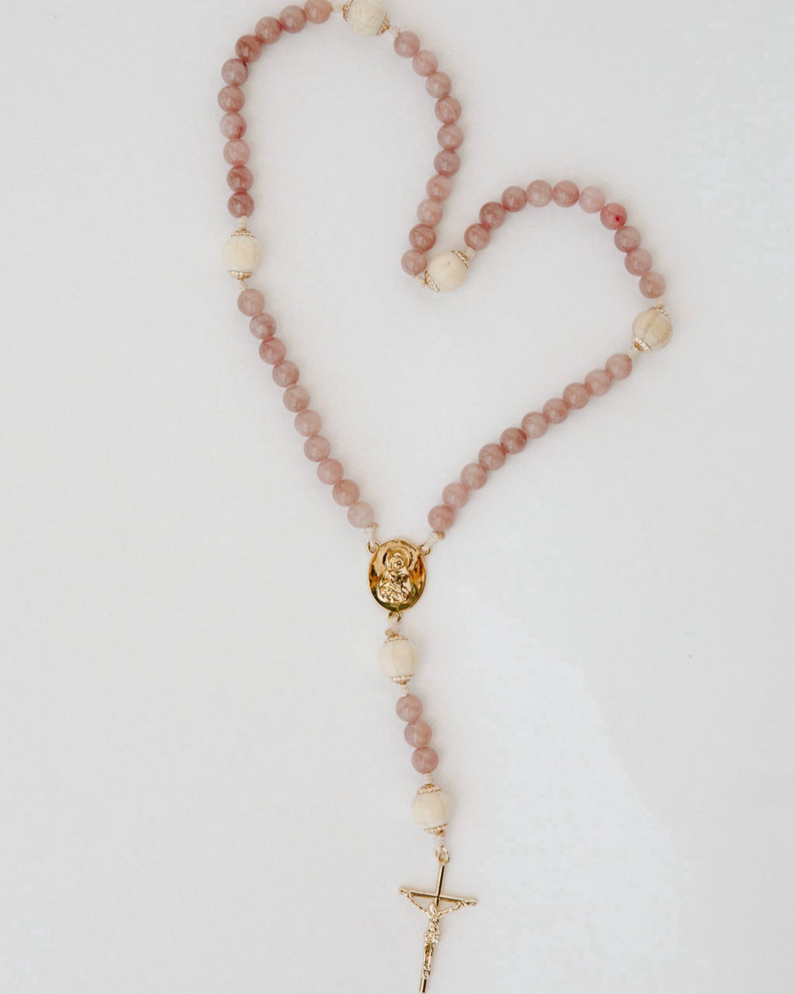 Rosary with pink and wood beads and a gold cross on a light gray background