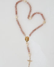 Rosary with pink and wood beads and a gold cross on a light gray background