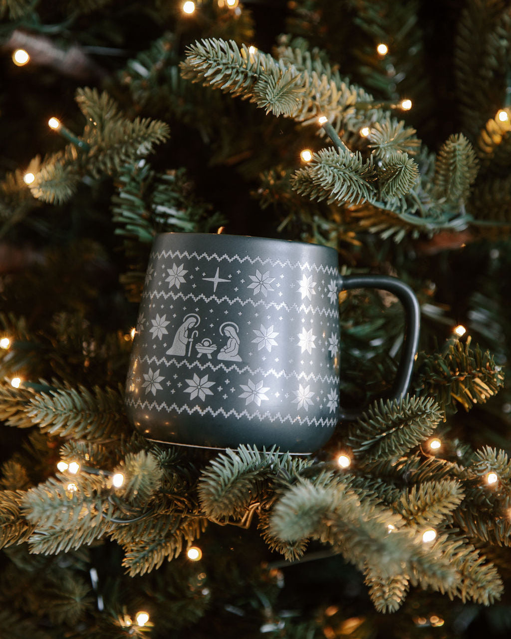 Decorative mug with snowflake patterns hanging on a Christmas tree with lights.