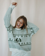 Woman wearing a patterned sweater with raised arms against a plain background