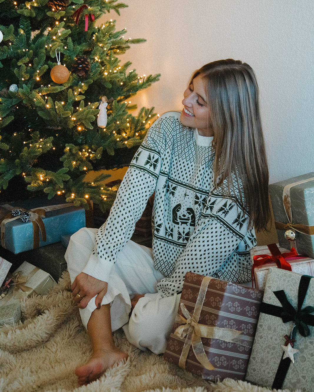 Woman sitting by a decorated Christmas tree with presents around her.