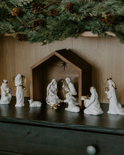 Nativity scene with white figures and a wooden stable under a Christmas tree.