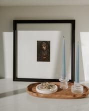 Framed artwork of our lady of sorrows a wall with candles and a wooden tray below