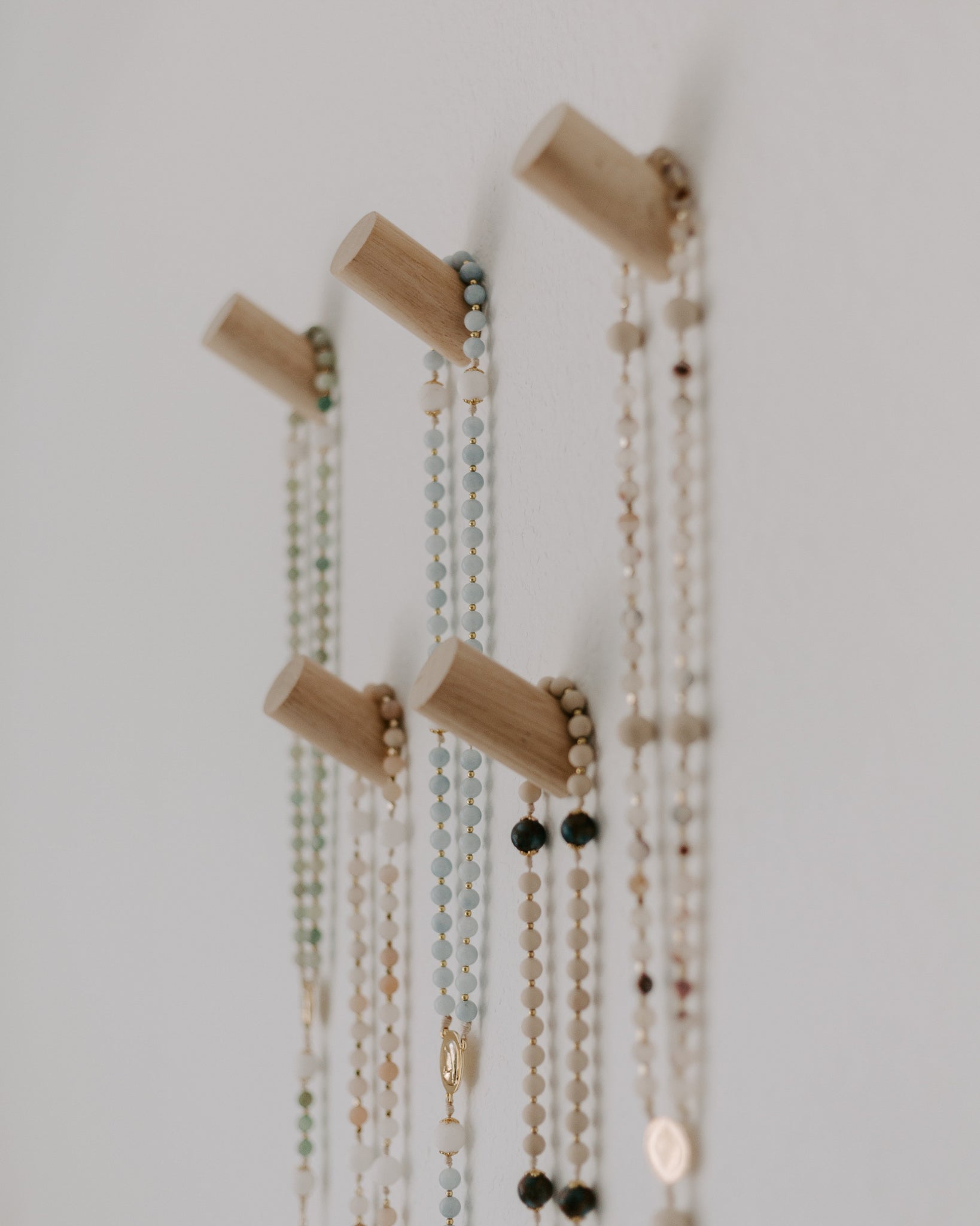 Rosary pegs with multiple necklaces hanging on a plain wall