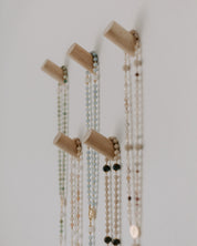 Rosary pegs with multiple necklaces hanging on a plain wall