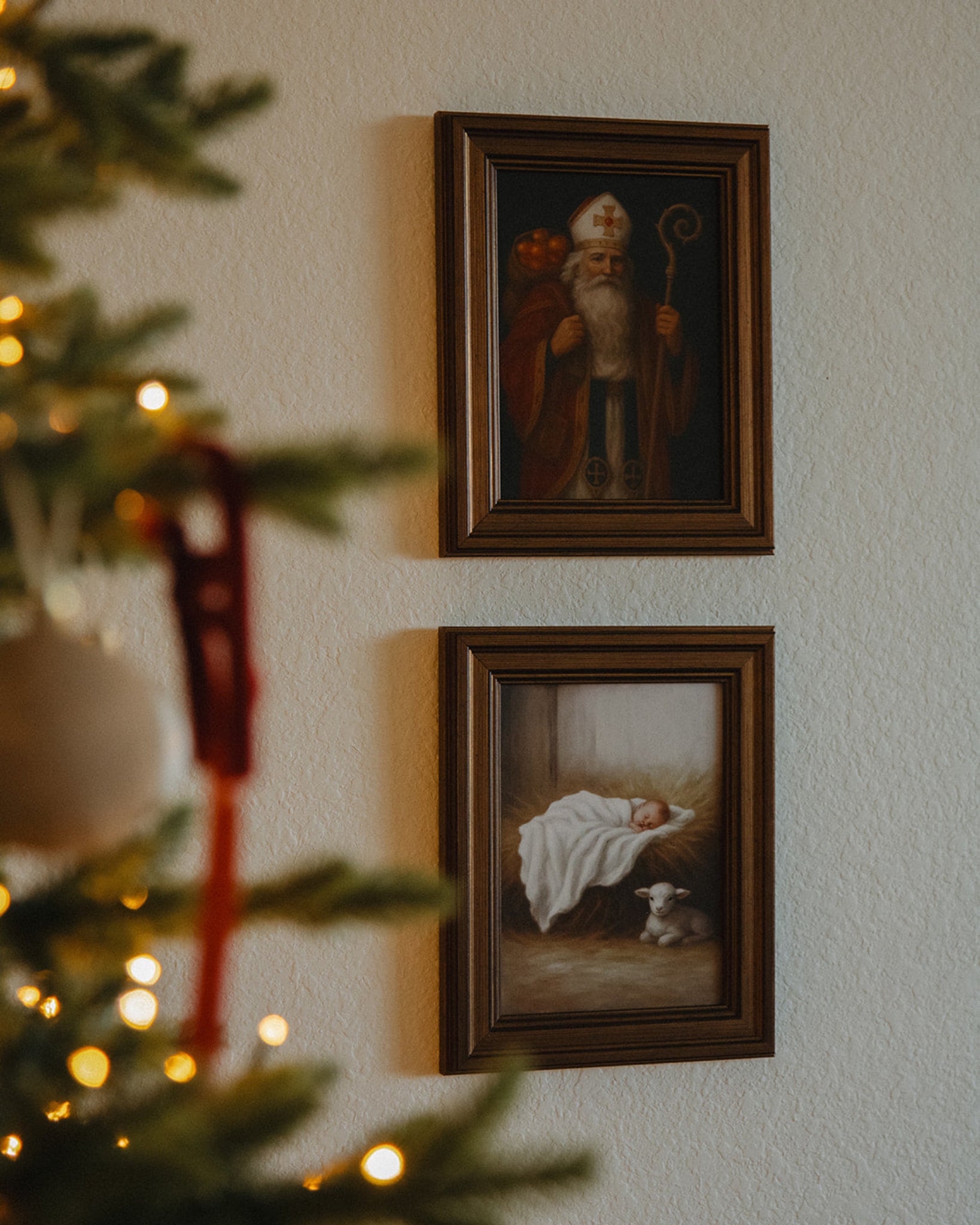 Two framed paintings on a wall with a Christmas tree in the foreground.
