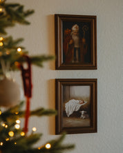 Two framed paintings on a wall with a Christmas tree in the foreground.