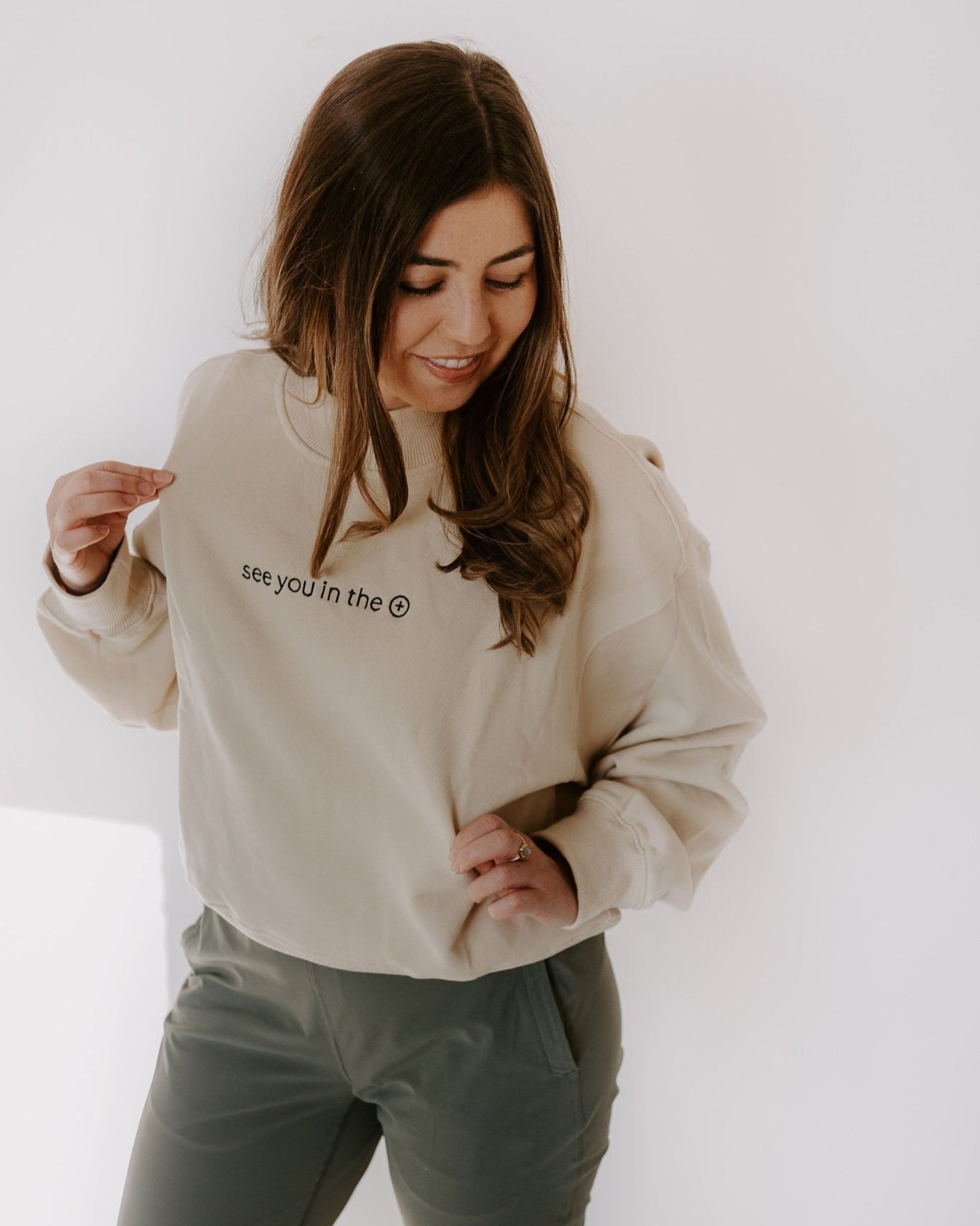 Woman wearing a beige sweatshirt with text on it against a white background