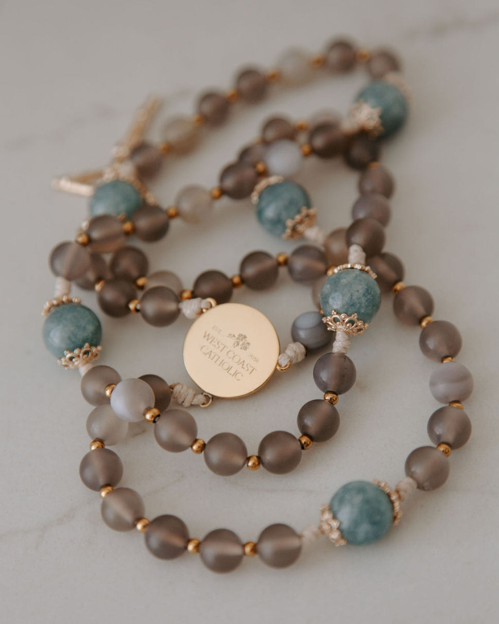 rosary with brown and blue beads with a gold medal detail on a white background