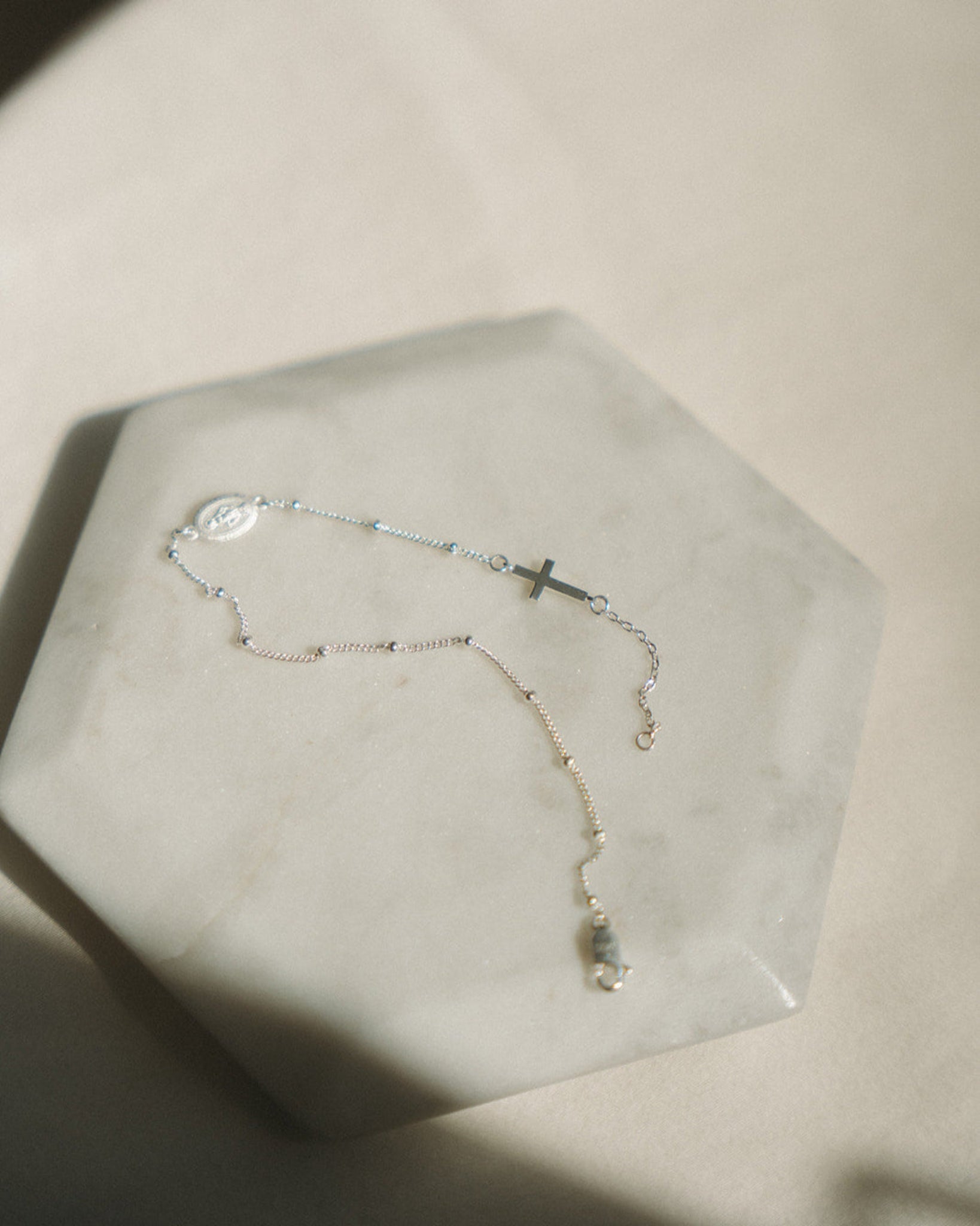 Silver rosary bracelet with a cross pendant on a hexagonal stone surface