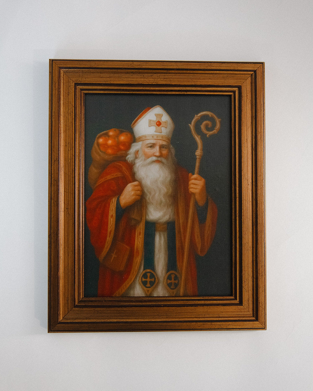 Framed painting of a robed figure with a staff and pumpkin on a white wall