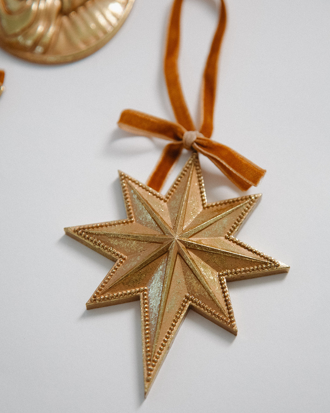 Gold star-shaped ornament with a brown ribbon on a light gray background