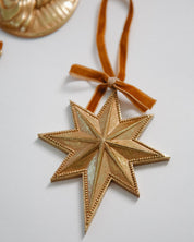 Gold star-shaped ornament with a brown ribbon on a light gray background
