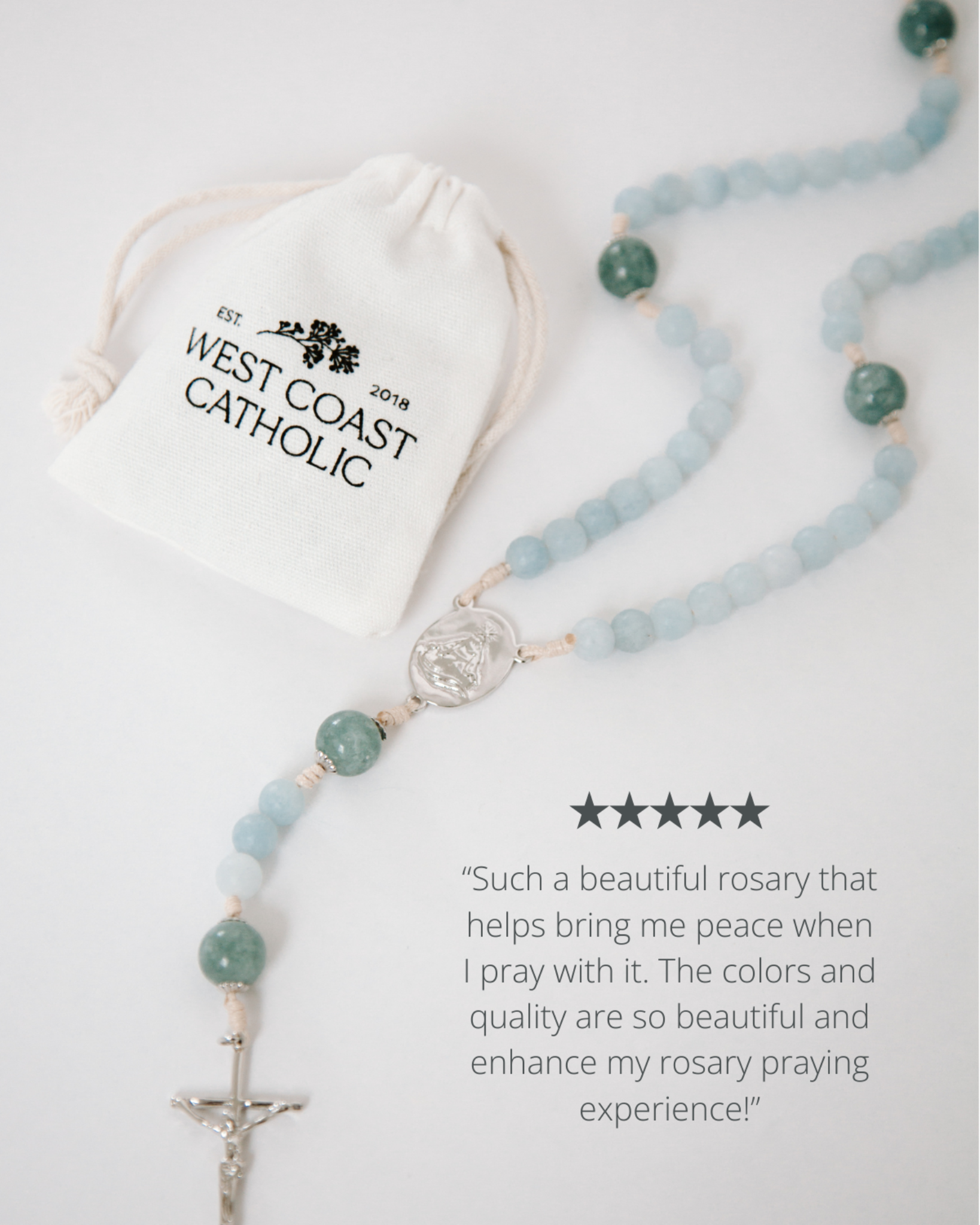 Rosary with blue beads and a silver cross on a white background, accompanied by a drawstring bag labeled 'West Coast Catholic'.