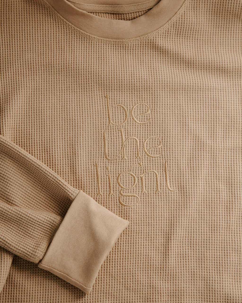 Beige long-sleeve shirt with 'be the light' text on a beige background