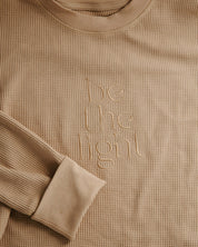 Beige long-sleeve shirt with 'be the light' text on a beige background
