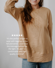 Person wearing a beige sweater with 'be the light' text, standing against a plain background.