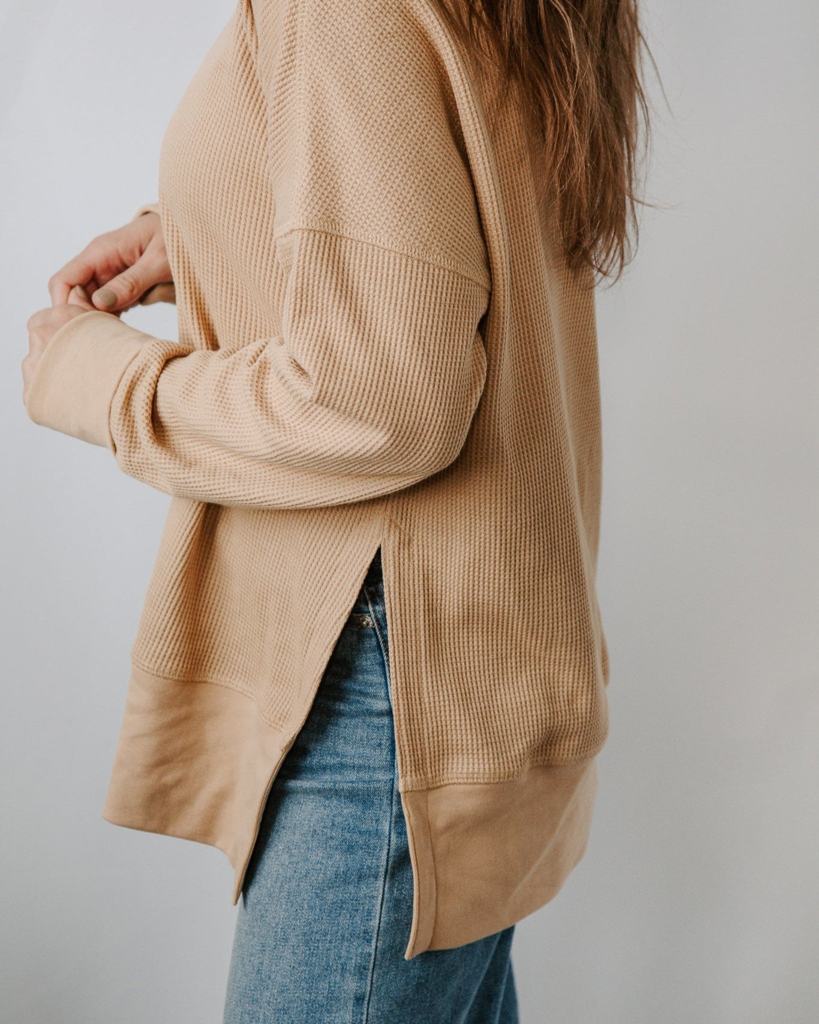 Person wearing a beige cardigan over a blue denim jacket on a plain background