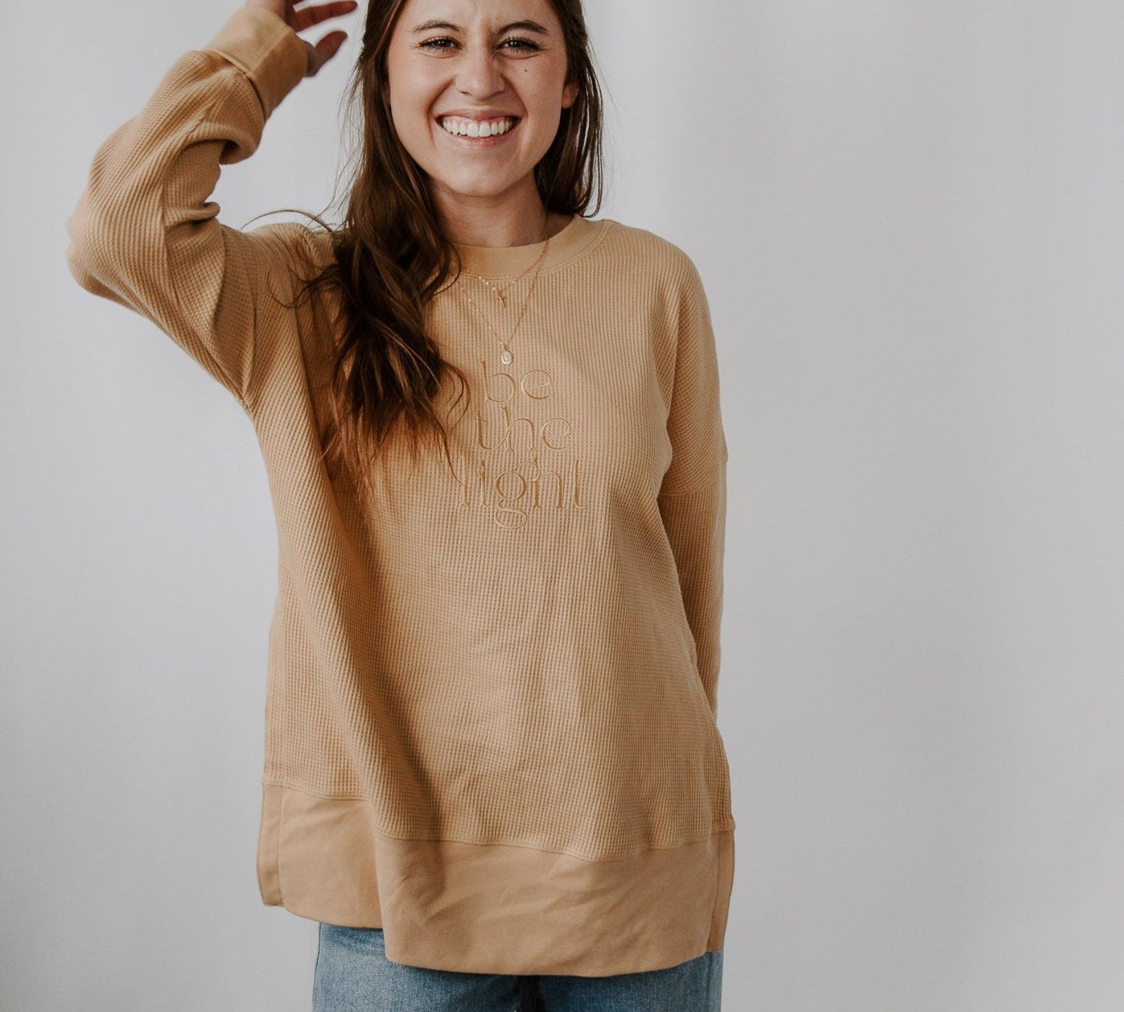 Woman wearing a beige sweater with text on it against a plain background