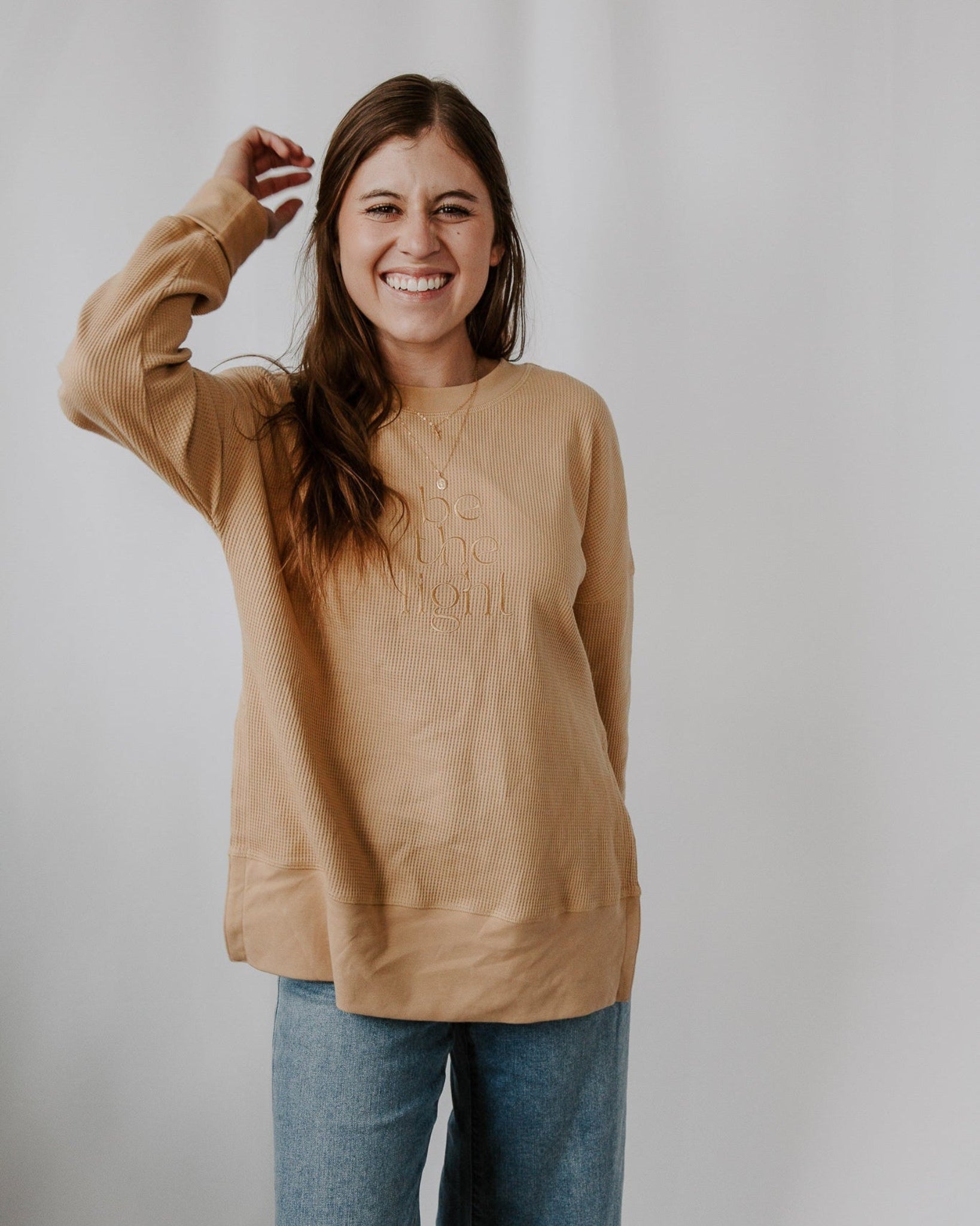 Woman wearing a beige sweater with text on it against a plain background