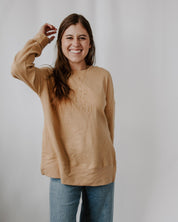 Woman wearing a beige sweater with text on it against a plain background