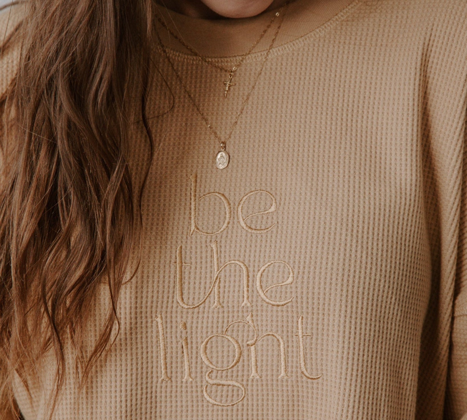 Person wearing a beige sweater with 'be the light' text, smiling.