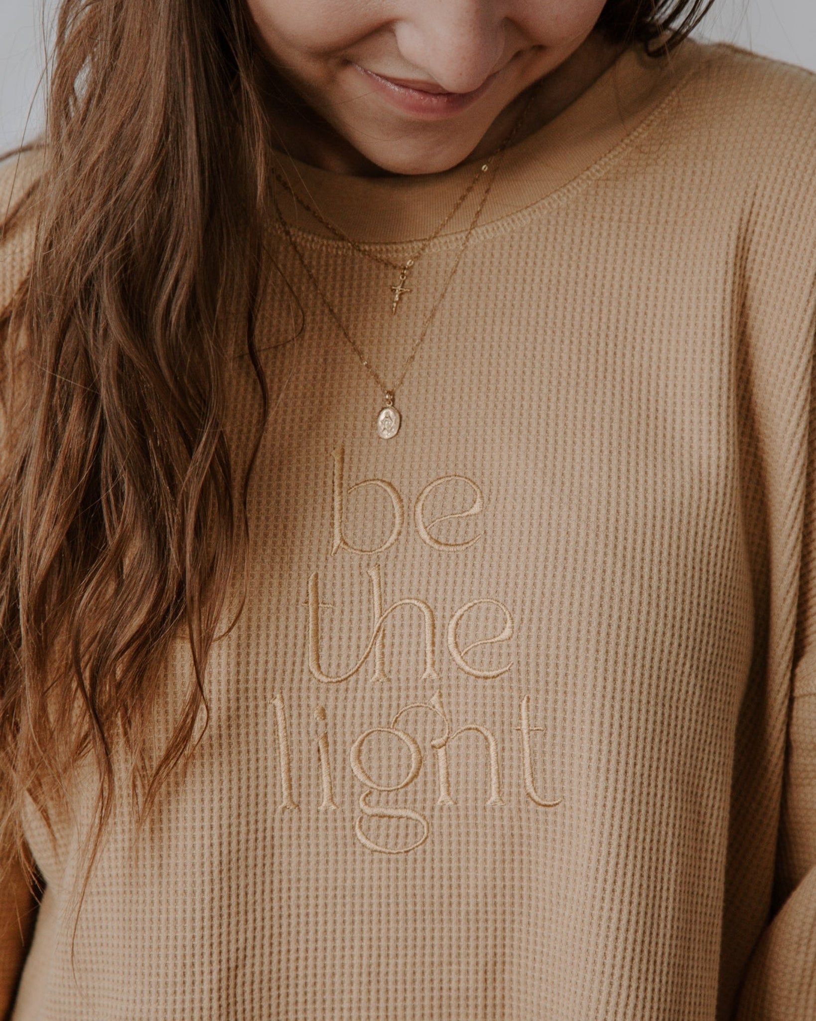Person wearing a beige sweater with 'be the light' text, smiling.