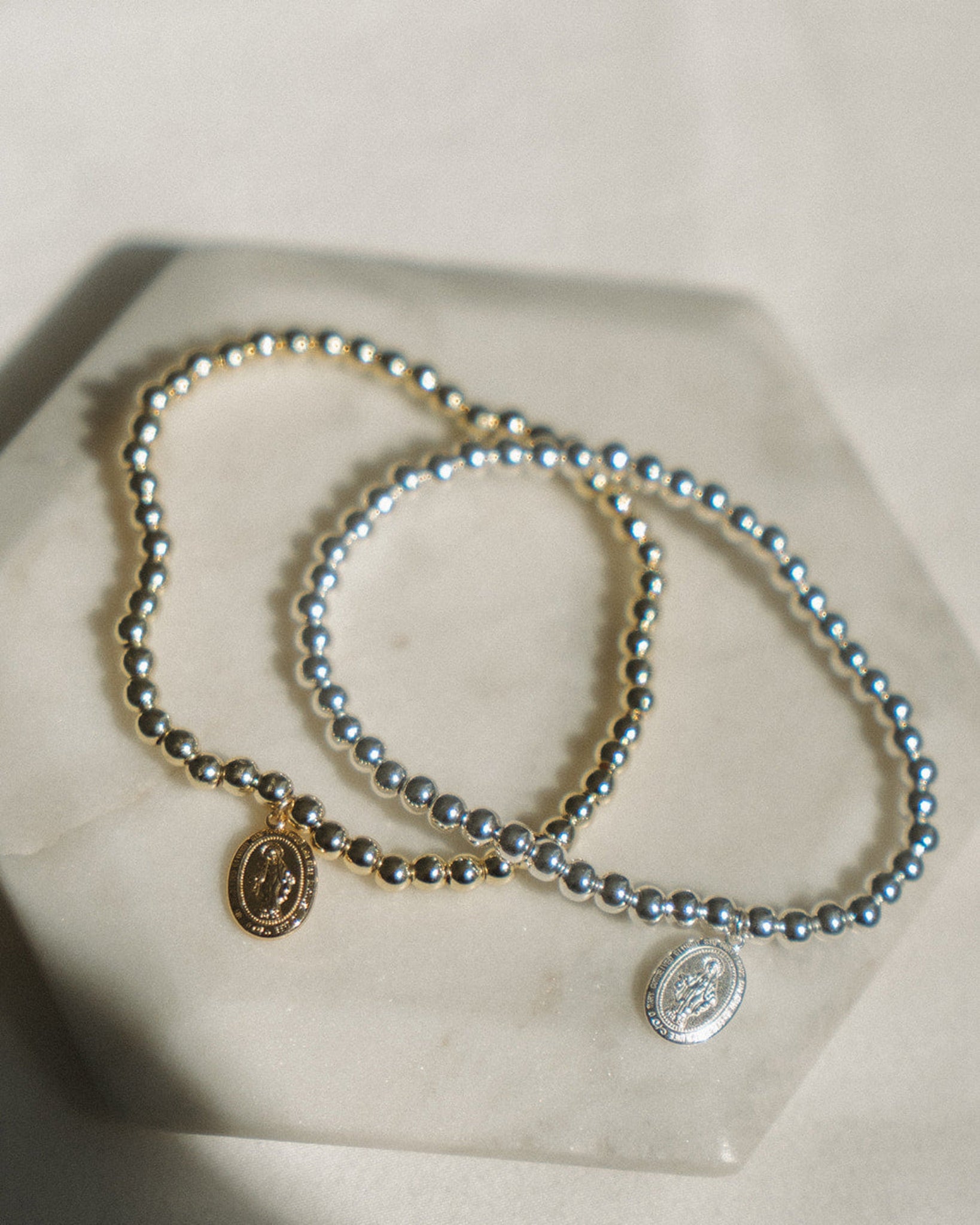 Two beaded bracelets with gold and silver Miraculous Medal on a light surface.