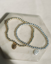Two beaded bracelets with gold and silver Miraculous Medal on a light surface.