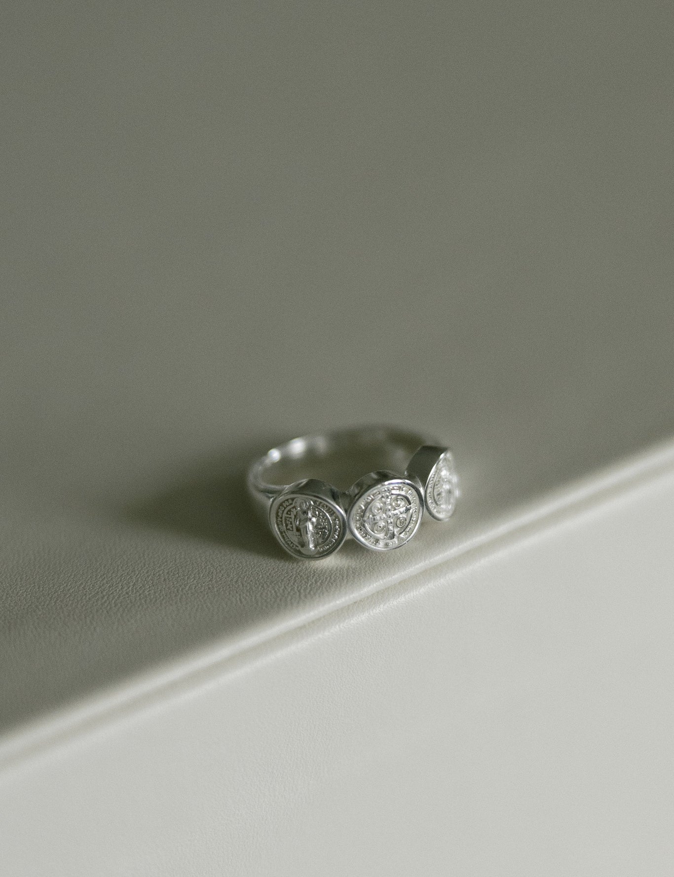 A silver St. Benedict ring, resting on a clean, light gray surface.