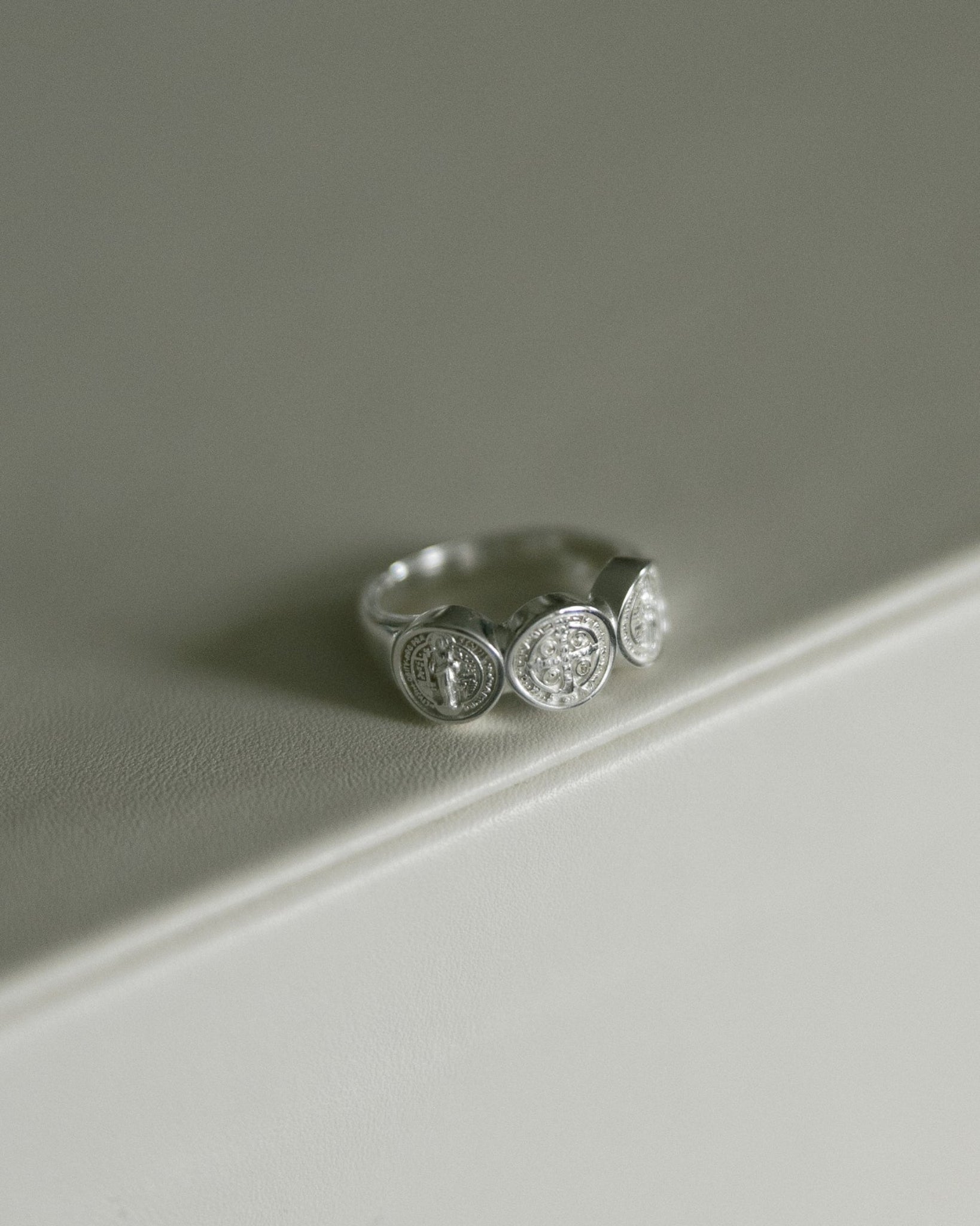 A silver St. Benedict ring, resting on a clean, light gray surface.