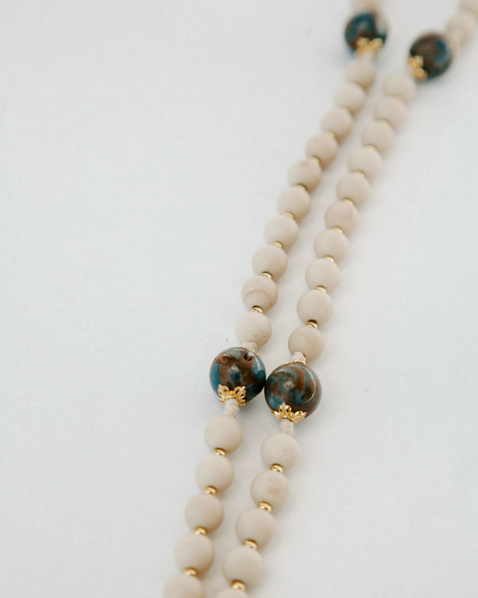 Beaded necklace with white beads and green and gold accents on a light gray background