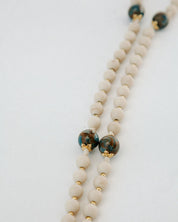Beaded necklace with white beads and green and gold accents on a light gray background