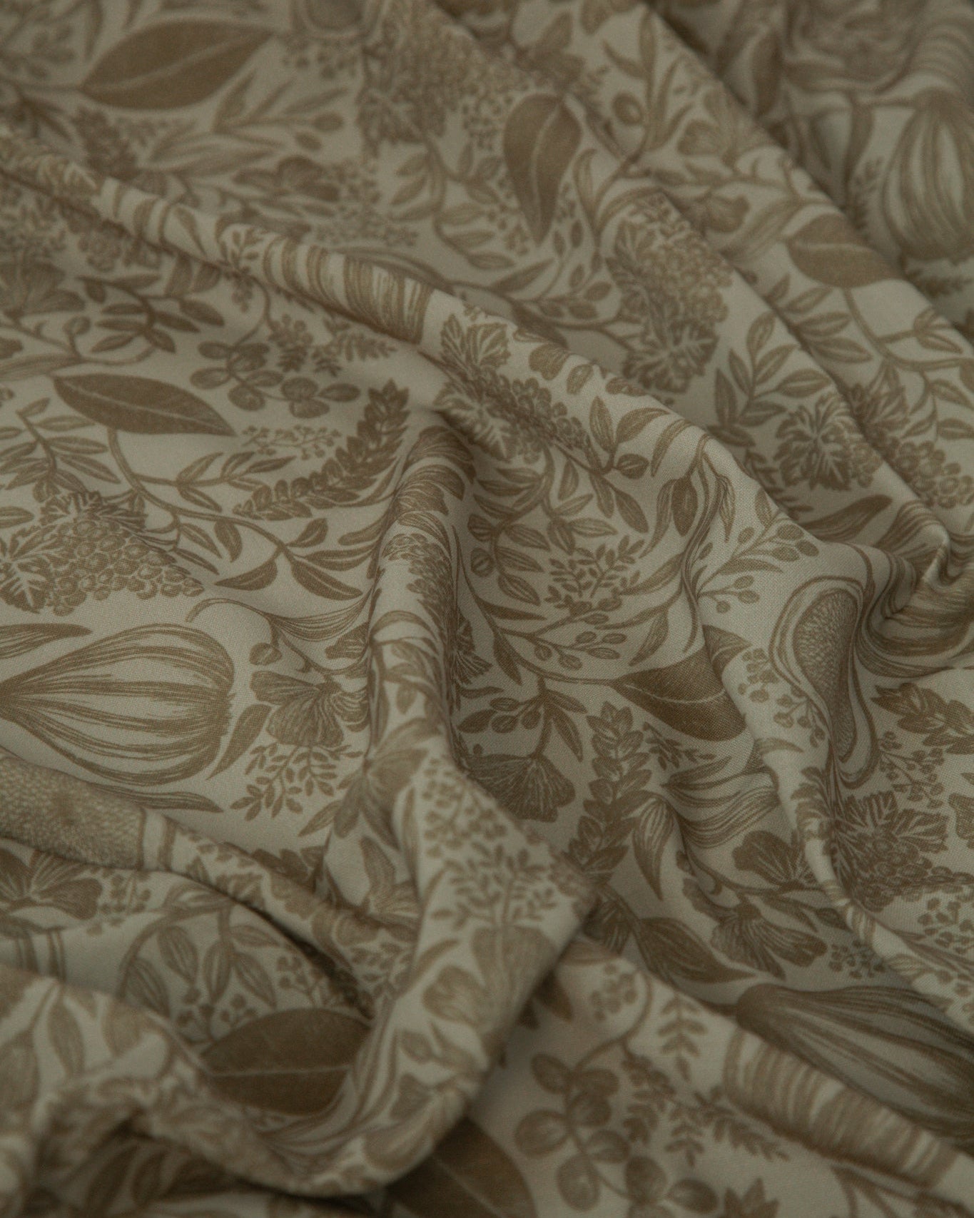A close-up of draped fabric with an all-over botanical print in warm taupe and beige tones.