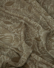 A close-up of draped fabric with an all-over botanical print in warm taupe and beige tones.