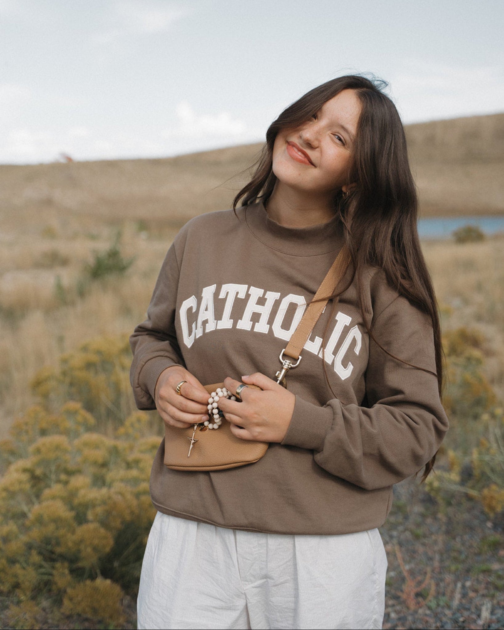 Person wearing a brown 'Catholic' sweatshirt in a field