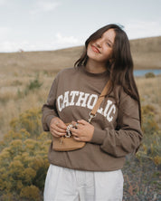 Person wearing a brown 'Catholic' sweatshirt in a field