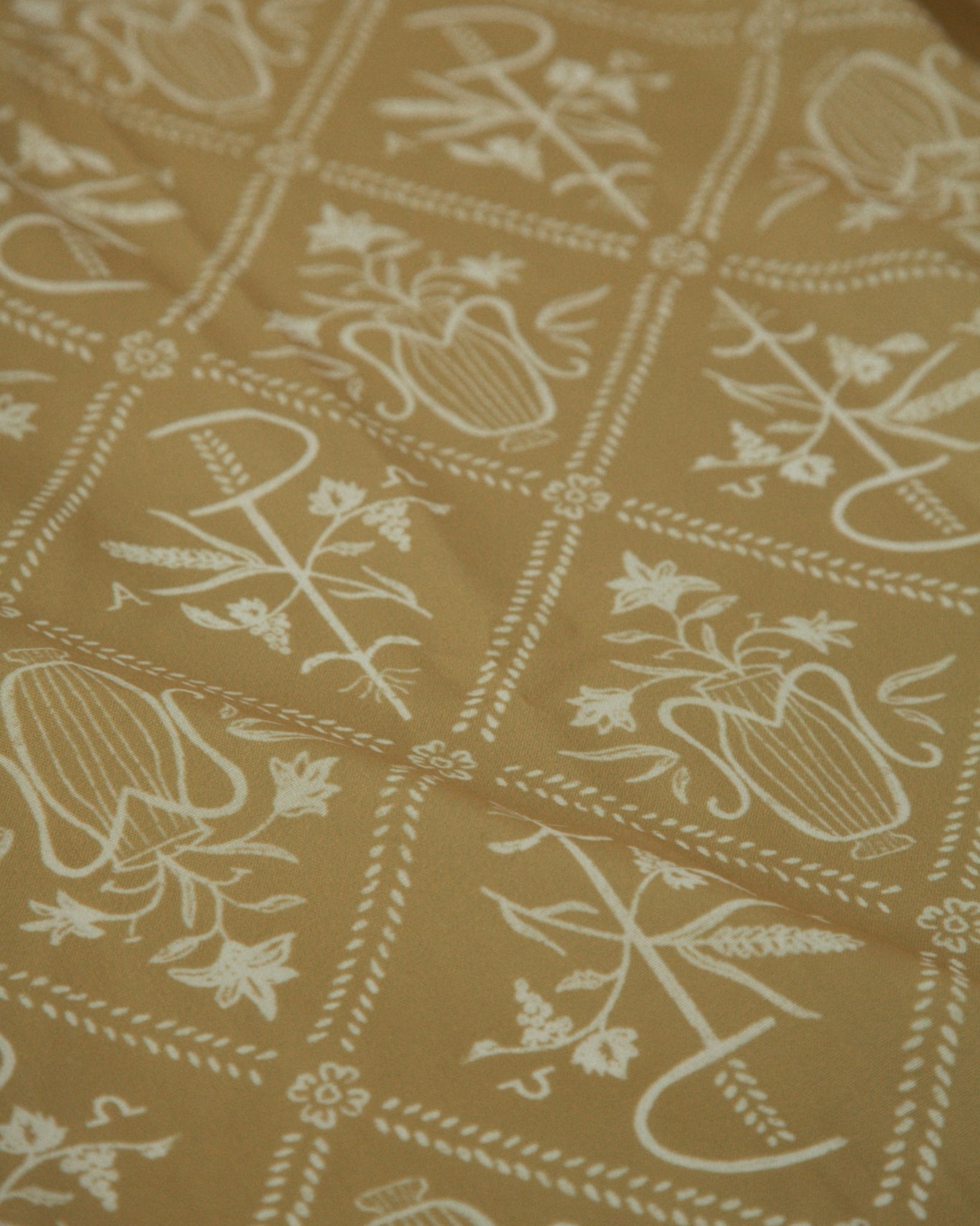 A close-up of a fabric or wallpaper pattern featuring white Chi Ro and floral symbol arranged in a grid on a warm mustard yellow background.