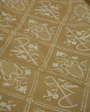 A close-up of a fabric or wallpaper pattern featuring white Chi Ro and floral symbol arranged in a grid on a warm mustard yellow background.