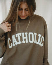 Person wearing a brown mockneck sweatshirt with 'CATHOLIC' printed on it.