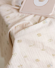 A close-up of a soft, pale blush muslin baby girl swaddle with a delicate repeating floral pattern.