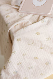 A close-up of a soft, pale blush muslin baby girl swaddle with a delicate repeating floral pattern.
