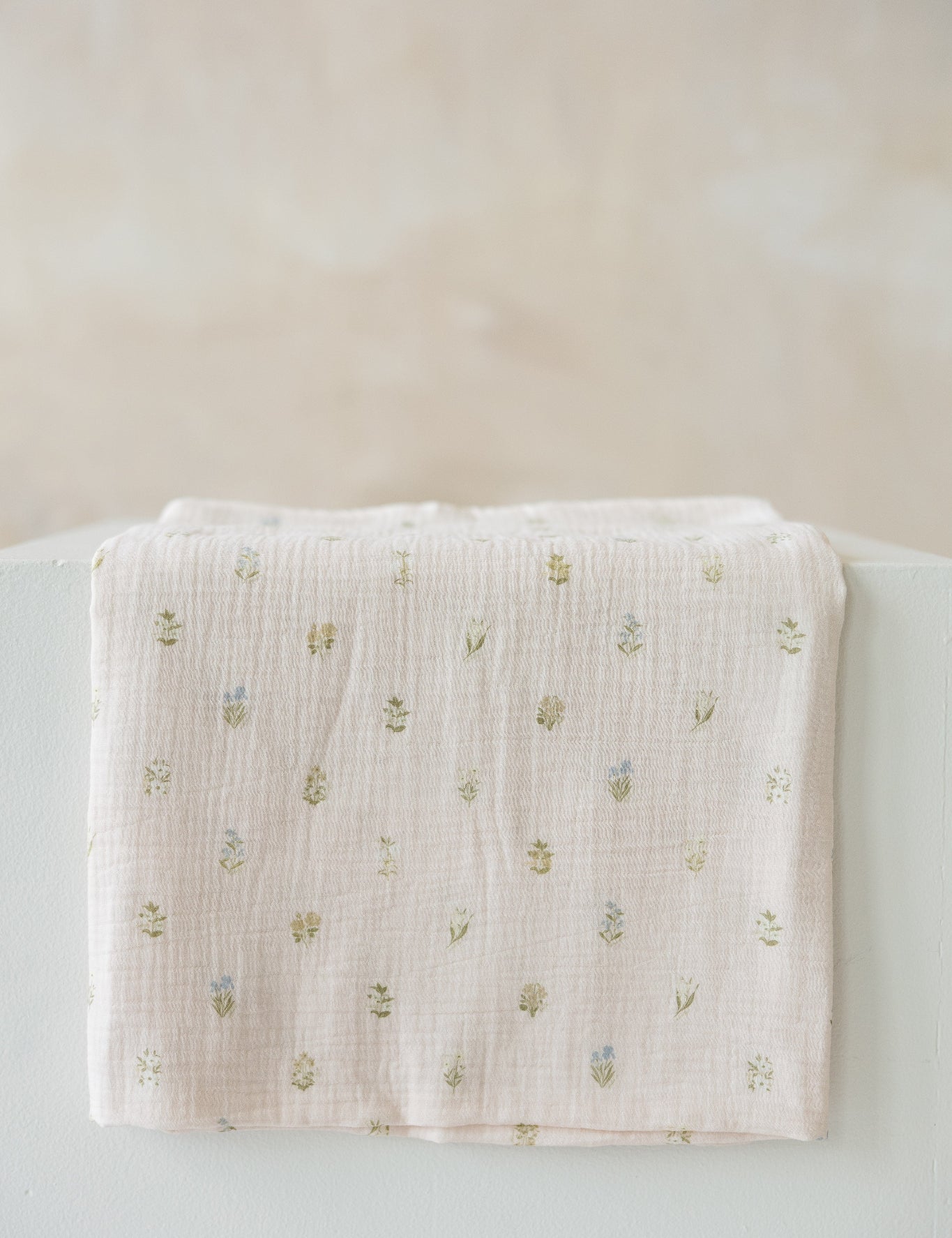 light pink muslin baby swaddle with a small embroidered floral pattern