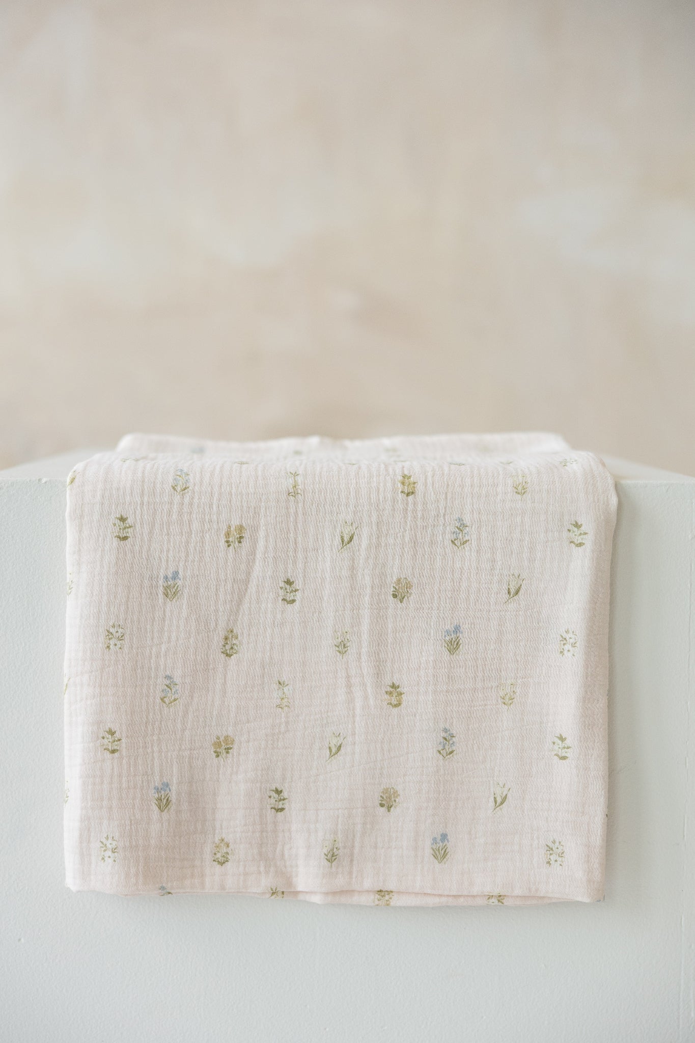light pink muslin baby swaddle with a small embroidered floral pattern