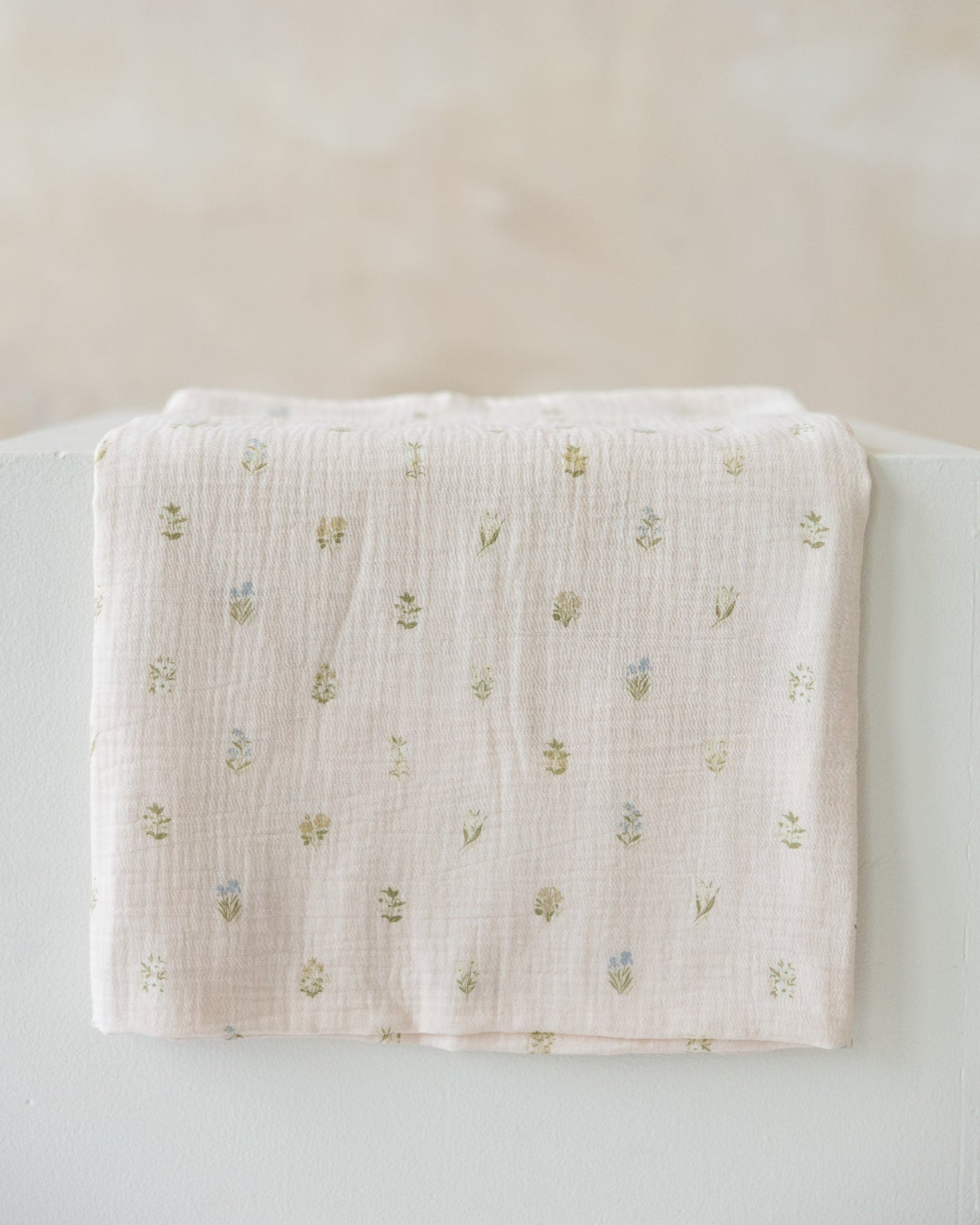 light pink muslin baby swaddle with a small embroidered floral pattern
