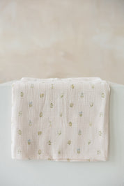 light pink muslin baby swaddle with a small embroidered floral pattern